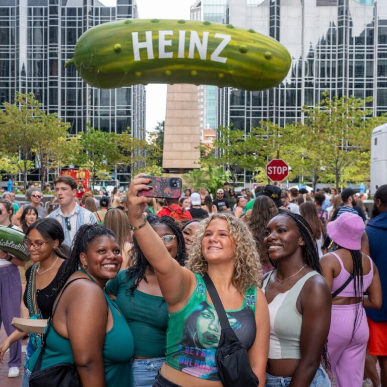 A group of women take a selfie in front of the Heinz inflatable pickle.