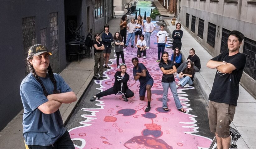 A group of artists taking a picture with the artwork they painted on the alley's concrete.