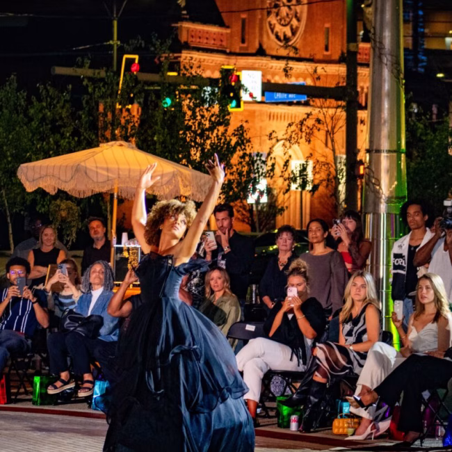 A woman dancing in the street at night with a crowd watching.