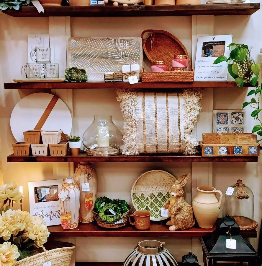 A set of shelves displaying various things for sale such as bars of soap, candles, desk organizers, pillows, and ornaments.