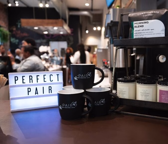 a stack of mugs on a coffee bar with a lit sign to the left that reads - Perfect Pair.