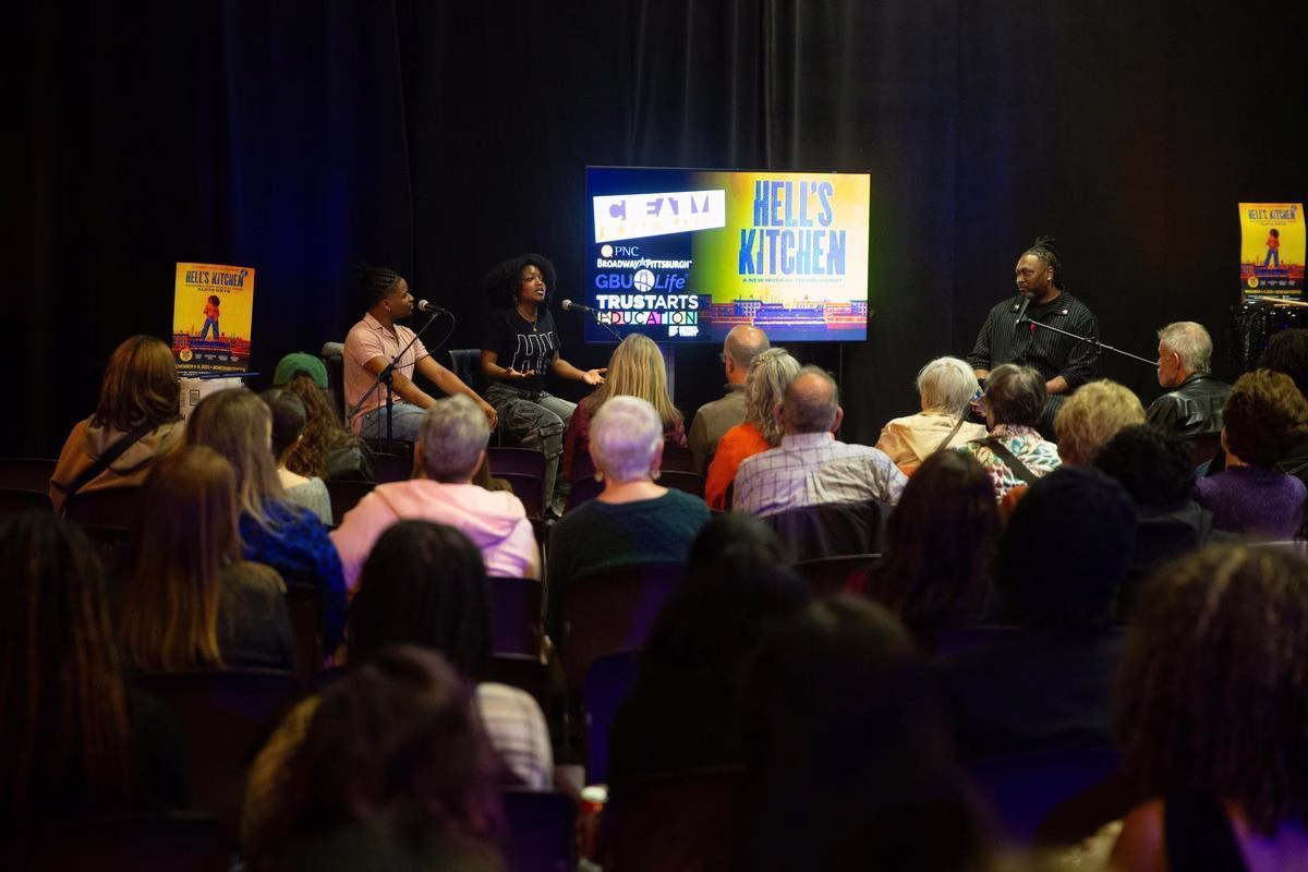 Three people on stage speak about Hell's Kitchen in front of an engaged audience.