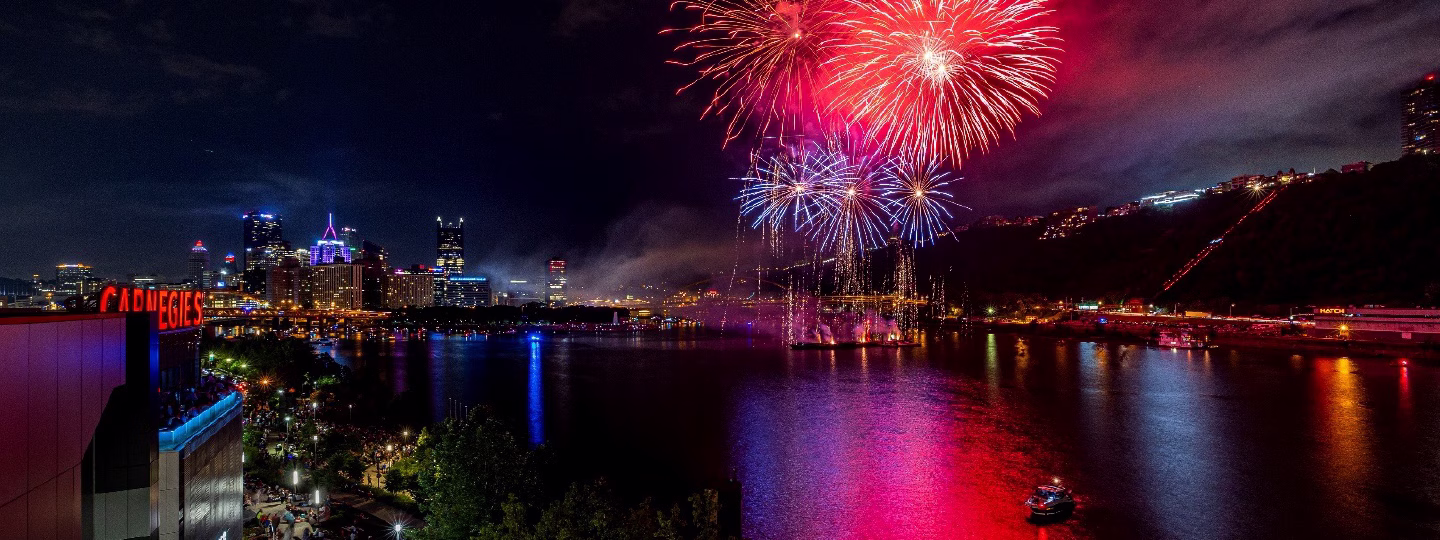 fireworks explode over Pittsburgh's confluence of rivers.